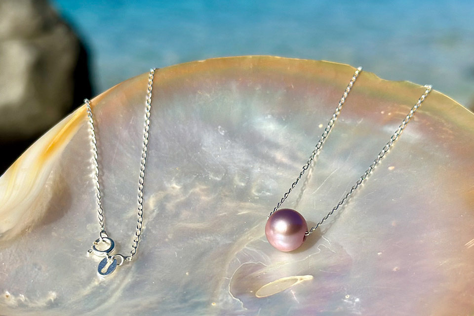 Chain necklace with a purple freshwater pearl displayed on mother-of-pearl
