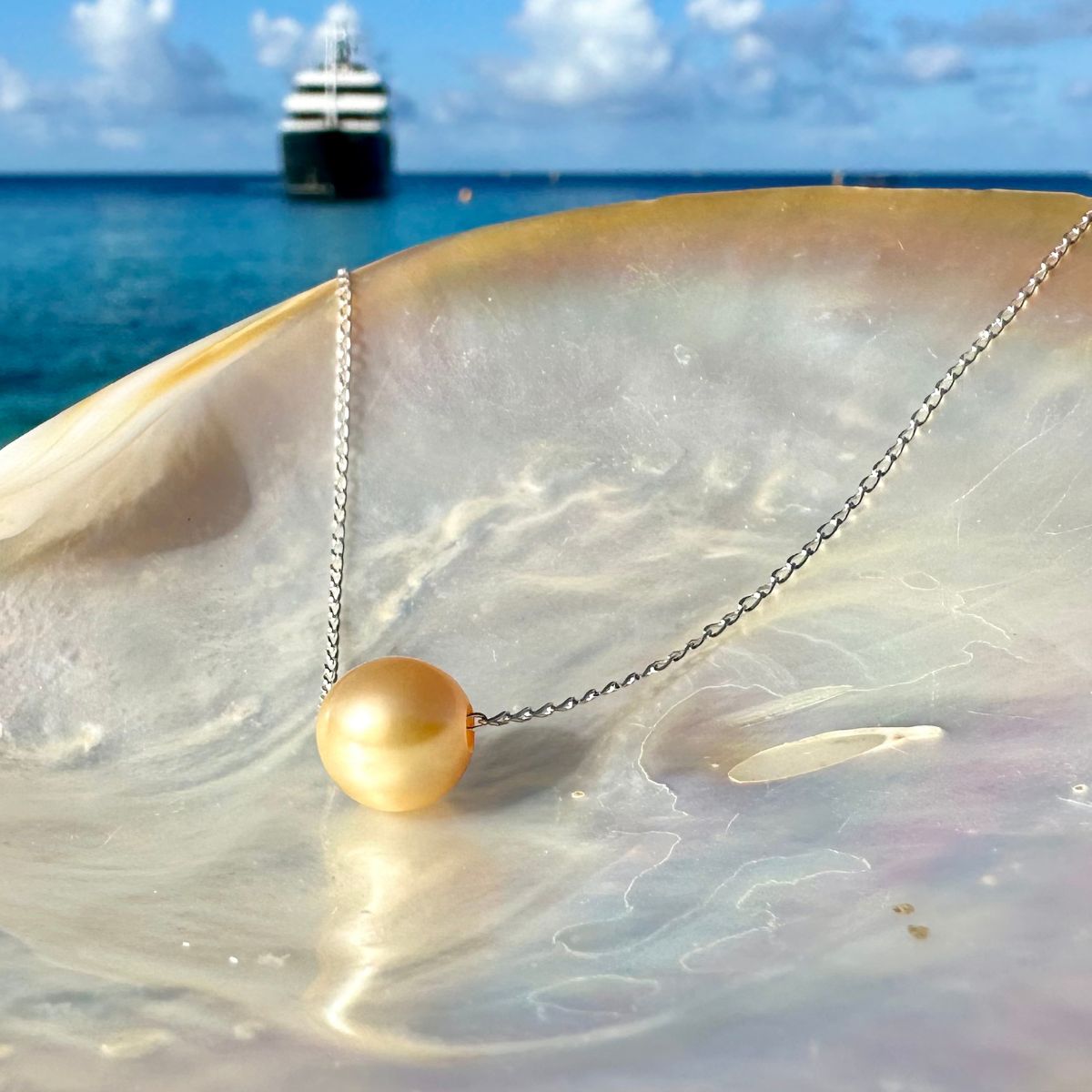 Chain necklace with a golden South Sea pearl displayed on mother-of-pearl by the sea