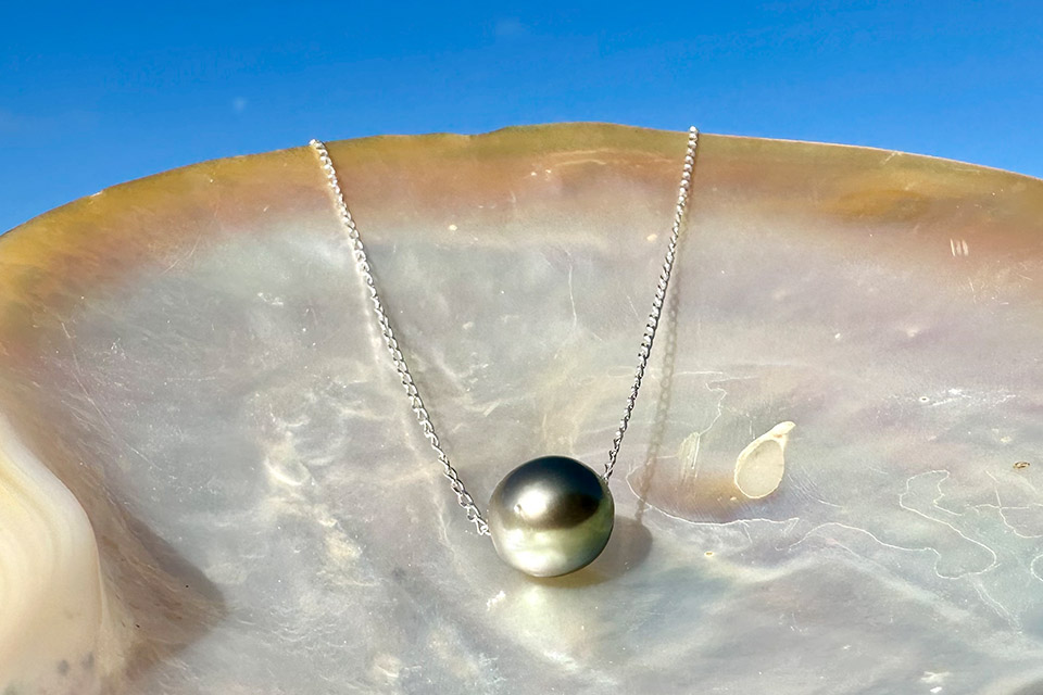 Chain necklace with a dark Tahitian pearl displayed on mother-of-pearl