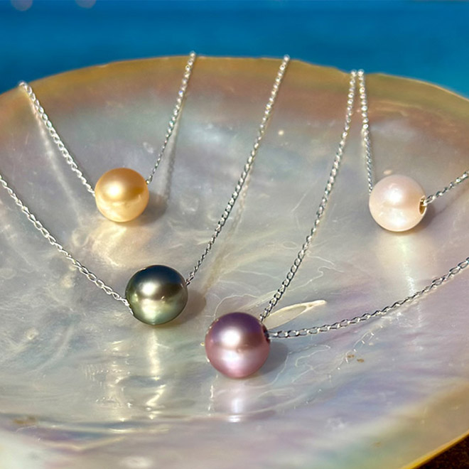 Four chain necklaces with white, golden, purple and Tahitian cultured pearls displayed on mother-of-pearl