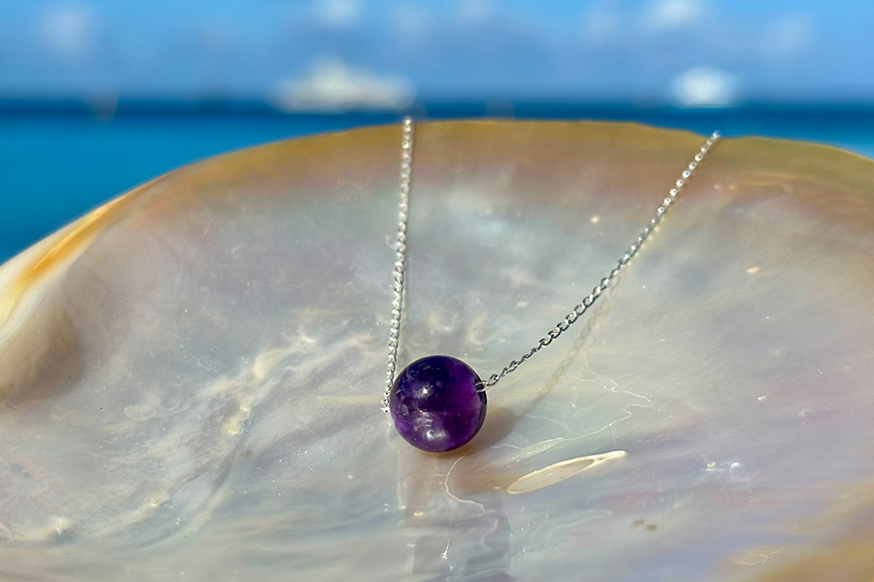 Silver chain necklace with a round amethyst displayed on mother-of-pearl