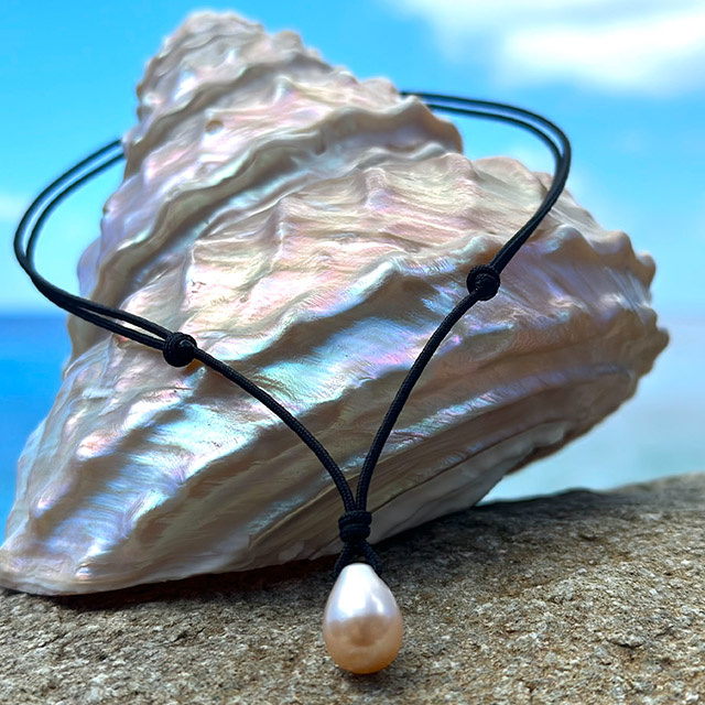Adjustable cord pendant necklace with a white drop-shaped freshwater cultured pearl on a black cord, displayed on a mother-of-pearl shell