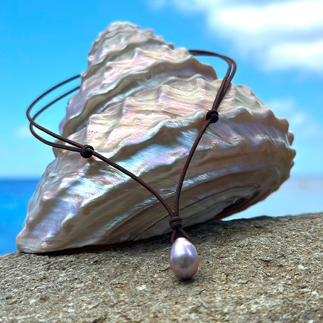 Adjustable cord pendant necklace with a pink drop-shaped freshwater cultured pearl on a brown cord, displayed on a mother-of-pearl shell