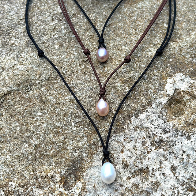 Three versions of the adjustable cord pendant necklace with drop-shaped freshwater cultured pearls displayed on rock