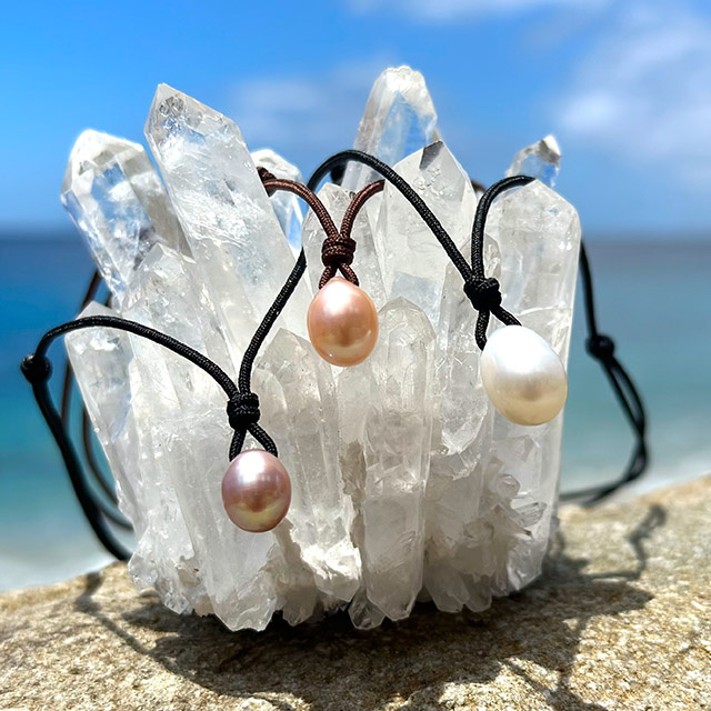 Three adjustable cord pendant necklaces with multicolored drop-shaped freshwater cultured pearls displayed on crystal