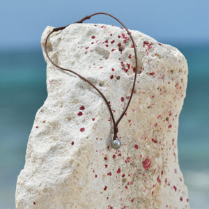 Unisex brown leather pendant necklace with two Tahitian cultured pearls displayed on a rock by the sea