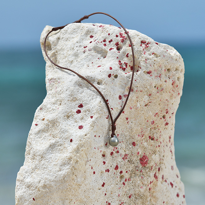 Unisex brown leather pendant necklace with two Tahitian cultured pearls displayed on a rock by the sea