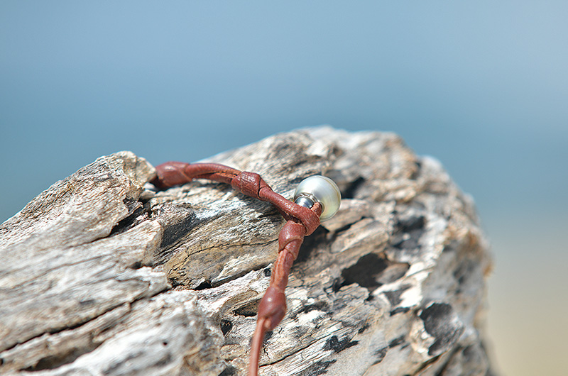 Detail of the brown leather knot on the Tahitian pearl pendant necklace displayed on driftwood