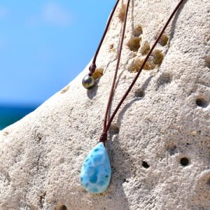 Adjustable brown leather pendant necklace with Larimar and a Tahitian cultured pearl displayed on a rock by the sea