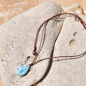 Full view of an adjustable brown leather pendant necklace with Larimar and a Tahitian cultured pearl arranged on a rock