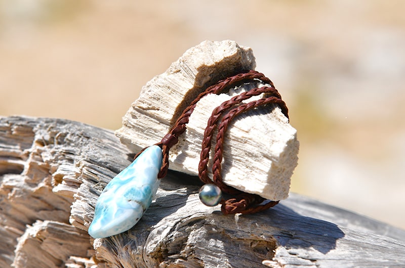 Braided leather necklace with a Larimar pendant and a cultured pearl clasp displayed on a rock