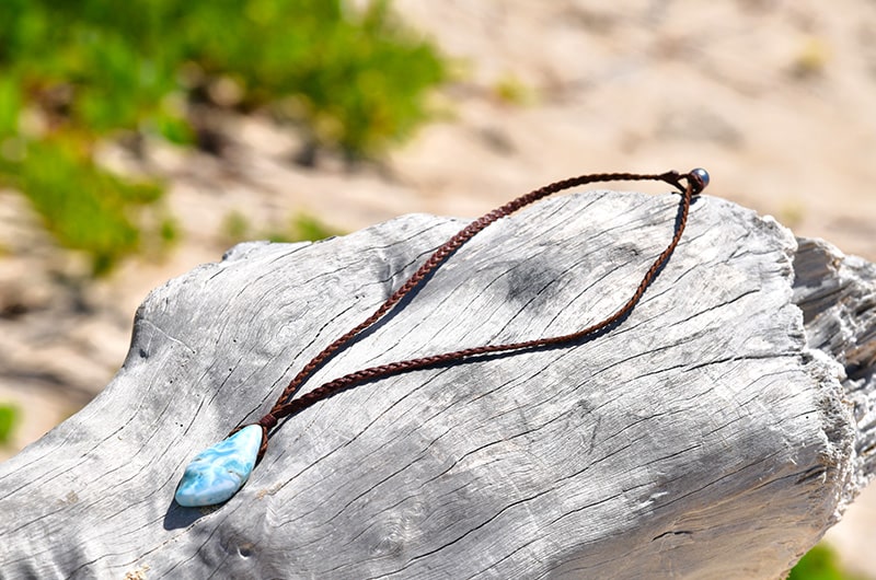 Braided leather necklace with a Larimar pendant arranged on driftwood