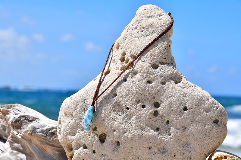 Full view of a braided kangaroo leather necklace with a Larimar pendant displayed on a rock by the sea