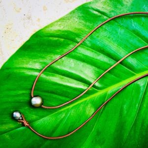 Adjustable brown leather choker necklace with two Tahitian cultured pearls displayed on a green leaf