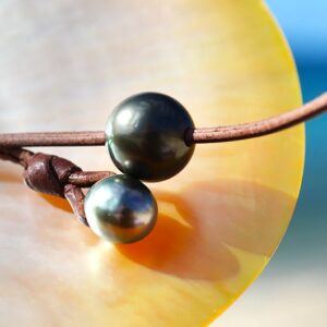 Detail of the two Tahitian cultured pearls and brown leather construction displayed on mother-of-pearl