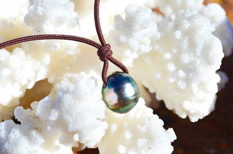 Gros plan sur la perle de culture de Tahiti de 10,5 mm du collier pendentif présentée sur du corail blanc
