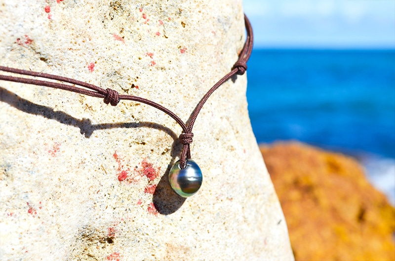 Détail des nœuds coulissants et de la perle de Tahiti de 10,5 mm du collier pendentif sur un rocher face à la mer