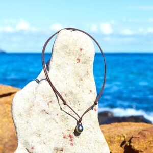 Full view of an adjustable brown cord pendant necklace with a 10.5 mm Tahitian pearl displayed on a rock by the sea