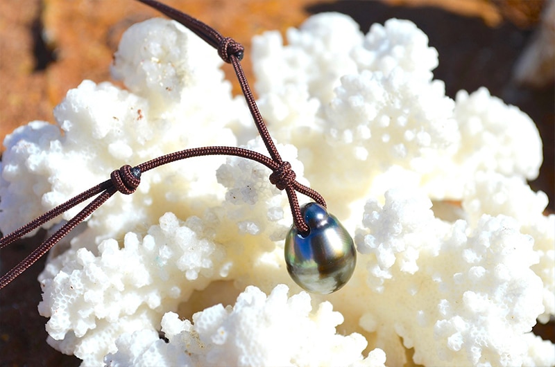 Gros plan sur la perle de culture de Tahiti de 12,5 mm du collier pendentif présentée sur du corail blanc
