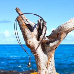 Full view of an adjustable brown cord pendant necklace with a 12.5 mm Tahitian pearl hanging from driftwood by the sea