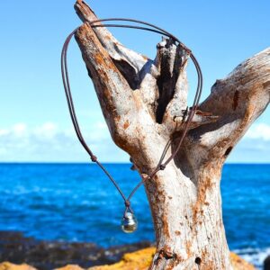 Adjustable brown cord pendant necklace with a 13.5 mm Tahitian cultured pearl hanging from driftwood by the sea