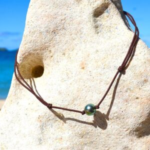 Adjustable choker necklace on a brown cord with a 9.5 mm semi-round Tahitian cultured pearl displayed on a rock facing the sea