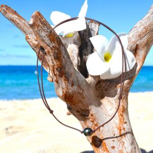 Adjustable choker necklace on a brown cord with a green 10.5 mm semi-round Tahitian cultured pearl displayed on driftwood facing the sea