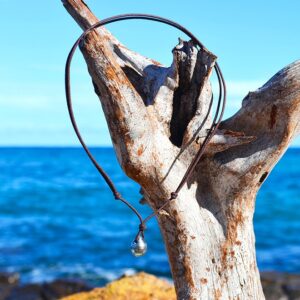 Adjustable pendant necklace on a brown cord with a 10 mm circled Tahitian cultured pearl displayed on driftwood facing the sea