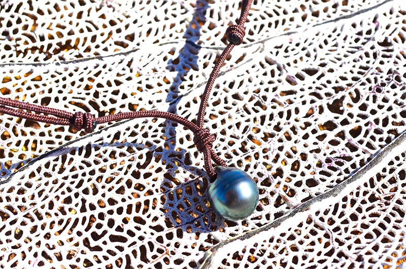 Détail de la perle de culture de Tahiti cerclée de 10 mm et du montage sur cordon marron présenté sur un support corallien