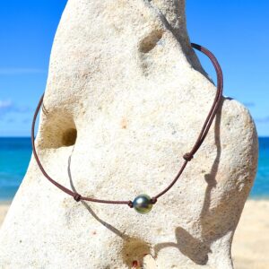 Adjustable choker necklace on a brown cord with a 10 mm semi-round Tahitian cultured pearl displayed on a rock facing the sea