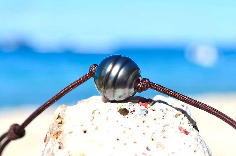 Gros plan sur la perle de culture de Tahiti de 11 mm et le cordon marron du collier ras du cou présentés sur du corail blanc