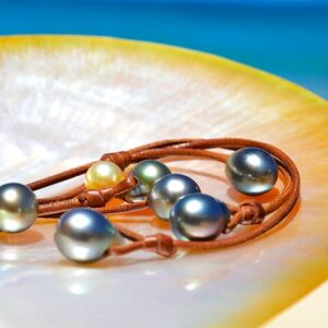 Gros plan sur les six perles de culture de Tahiti et la perle dorée des mers du Sud du collier tressé présentées face à la mer