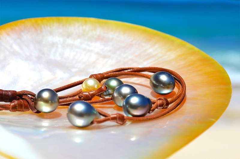 Gros plan sur les six perles de culture de Tahiti et la perle dorée des mers du Sud du collier tressé présentées face à la mer
