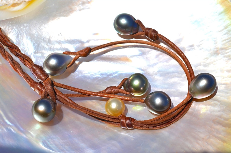 Détail des perles de culture de Tahiti, de la perle dorée des mers du Sud et du cuir tressé du collier présentés sur une nacre