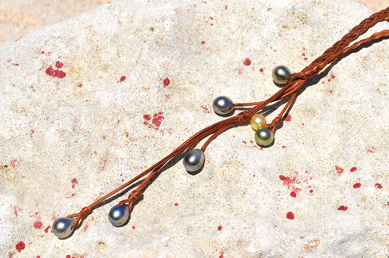 Vue rapprochée du collier en cuir tressé avec six perles de Tahiti et une perle dorée des mers du Sud disposé sur une roche claire