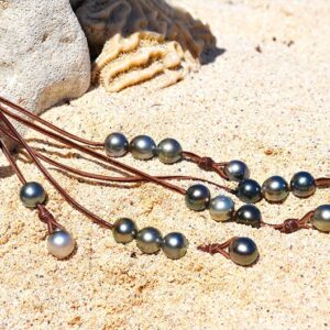 Sautoir en cuir tressé avec 33 perles de culture de Tahiti déployé sur le sable près d’un support corallien