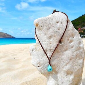 Full view of the braided leather necklace with turquoise and a Tahitian cultured pearl displayed on a coral stand at the beach