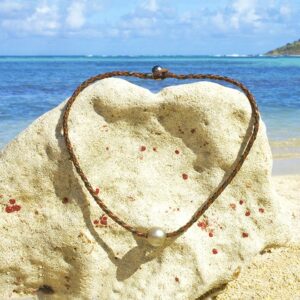 Braided leather choker necklace with two Tahitian cultured pearls displayed on a coral stand facing the sea