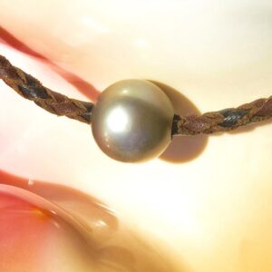 Detail of a Tahitian cultured pearl and the braided leather choker necklace displayed on a pink seashell