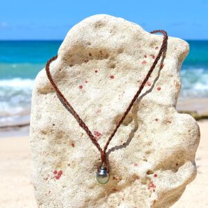 Braided leather pendant necklace with two baroque Tahitian cultured pearls displayed on a coral stand facing the sea