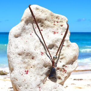 Braided leather necklace with Celestial Eye obsidian and a Tahitian cultured pearl displayed on a coral stand facing the sea