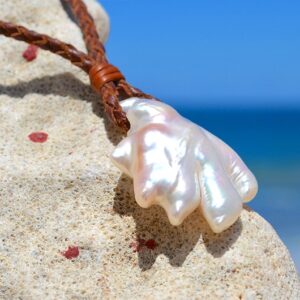 Collier pendentif tressé avec une grande perle de culture d’eau douce baroque présenté sur une roche face à la mer