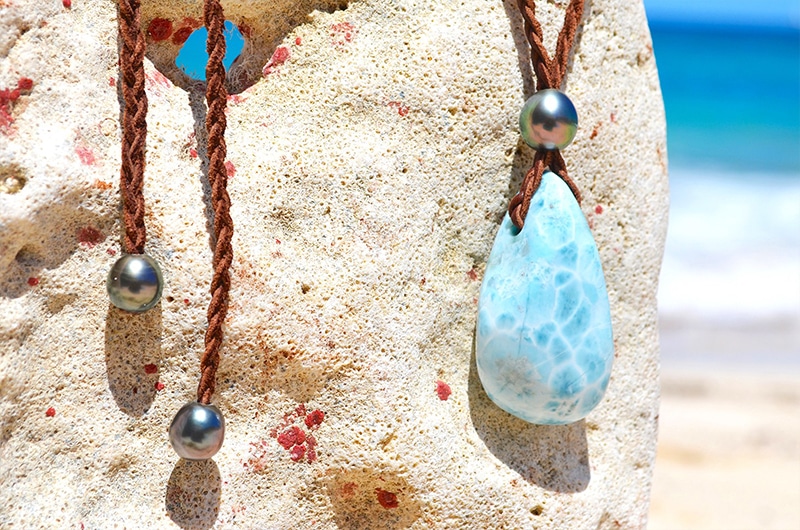 Autre vue du collier pendentif tressé avec un Larimar et quatre perles de culture de Tahiti présenté sur une roche face à la mer