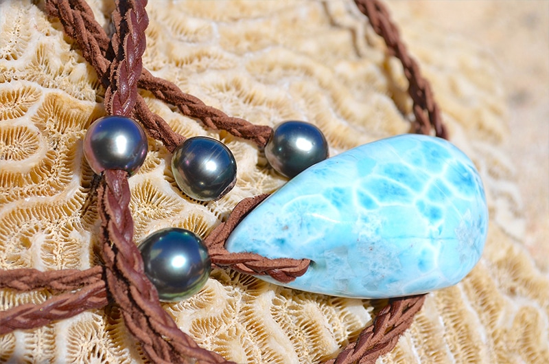 Gros plan sur le Larimar, les quatre perles de culture de Tahiti et le cuir tressé du collier présentés sur du corail