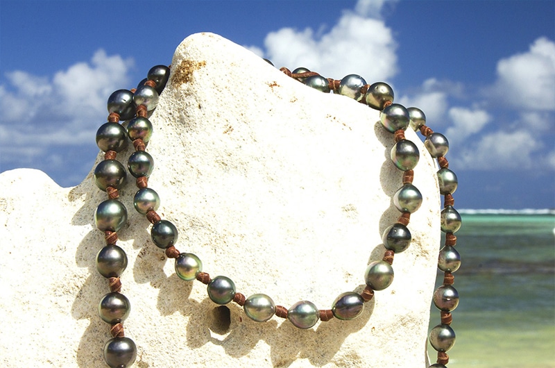Vue rapprochée du sautoir avec 68 perles de culture de Tahiti disposé sur un support corallien face à la mer