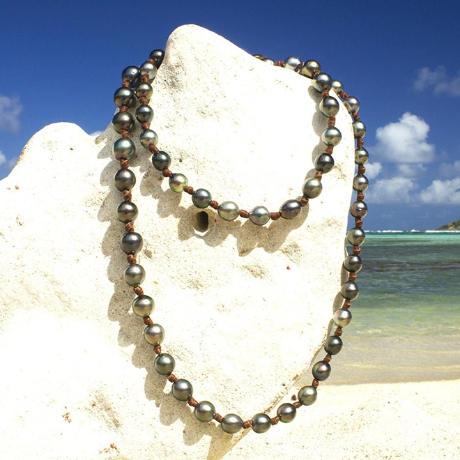 Vue d’ensemble du sautoir en cuir avec 68 perles de culture de Tahiti présenté sur un support corallien à la plage