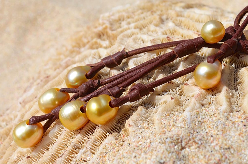 Detail of the seven South Sea cultured pearls and brown leather setting on the necklace displayed on coral