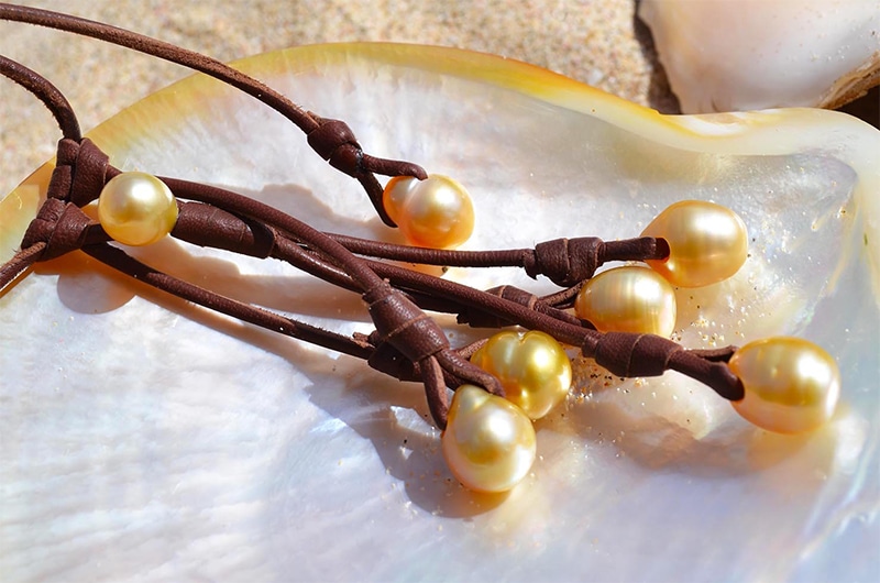 Close-up of the seven South Sea cultured pearls and brown leather on the necklace arranged on mother-of-pearl