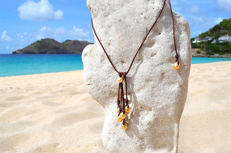 Full view of the adjustable leather necklace with a cluster of seven South Sea cultured pearls displayed on a coral stand at the beach