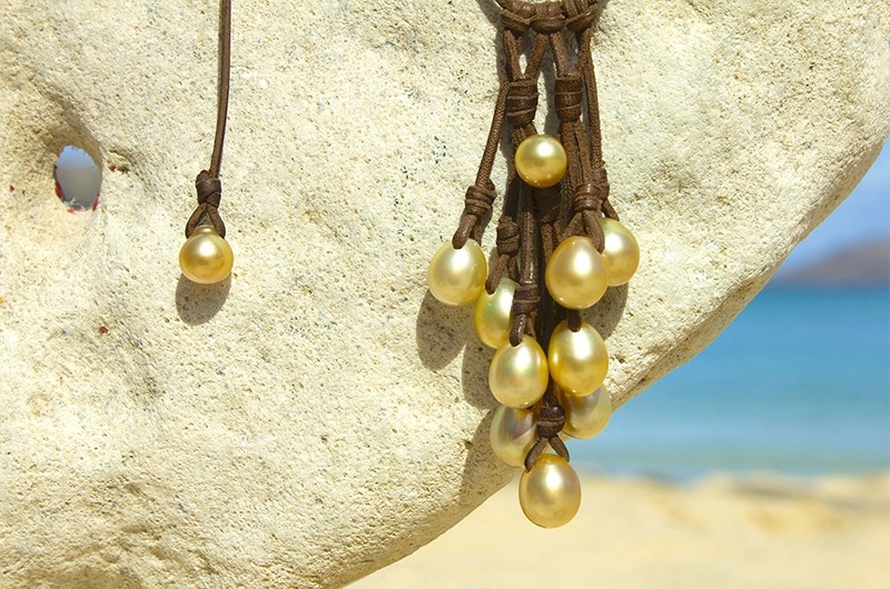 Alternate view of the cluster of 11 golden South Sea cultured pearls hanging in front of a rock at the beach
